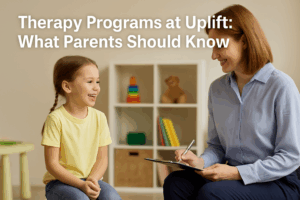 A smiling young girl sits in a therapy session with a friendly female therapist in a bright, child-friendly room. The therapist holds a clipboard and engages warmly with the child, symbolizing supportive pediatric care.