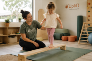 A pediatric occupational therapist at Uplift Therapy Center guides a smiling young child across a colorful balance beam in a bright, modern sensory gym near Pasadena, CA.